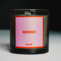 Black candle with a pink and red label featuring the candle name 'MENNO' and the brand name 'koyd' on a dark background